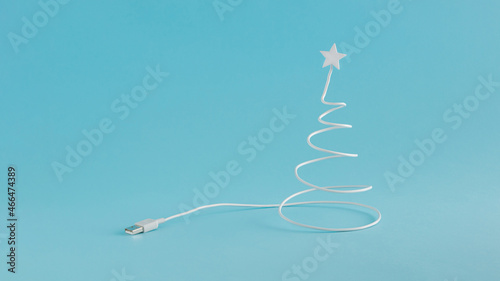 Creative digital Christmas arrangement made of USB cable in the shape of a Christmas tree on a blue background. Minimal New Year concept with copy space. Online holiday inspiration.