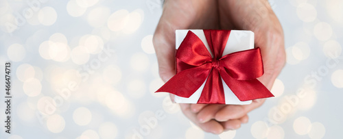Woman hands holding christmas present closeup, gift box with red ribbon over bright background panoramic banner. Christmas greeting card, birthday present, winter holidays, celebration concept