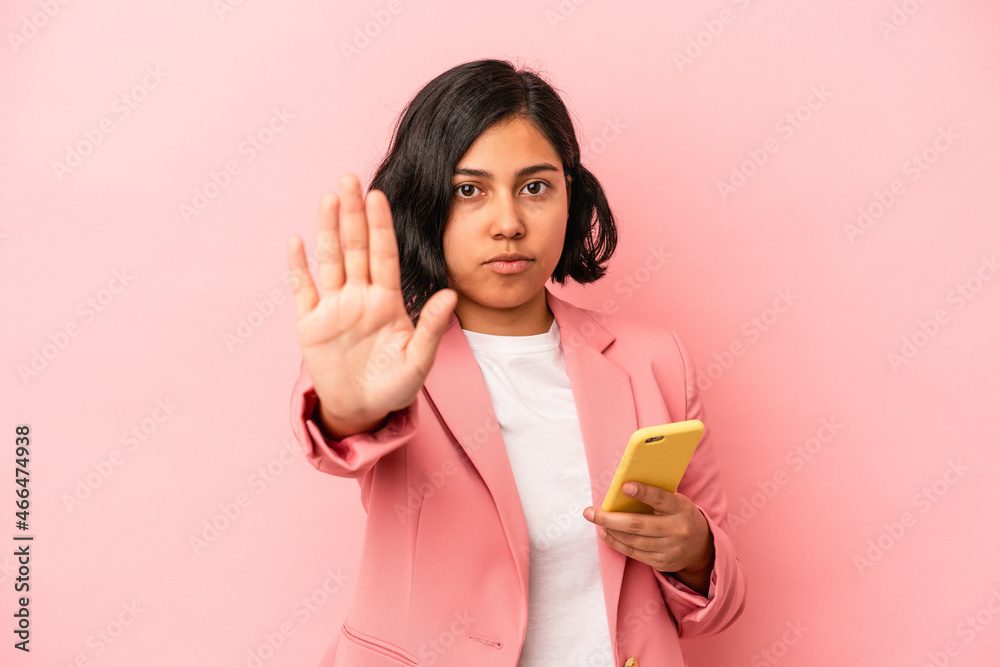 Young latin woman holding mobile phone isolated on pink background standing with outstretched hand showing stop sign, preventing you. Young latin woman holding mobile phone isolated on pink background standing with outstretched hand showing stop sign, preventing you.