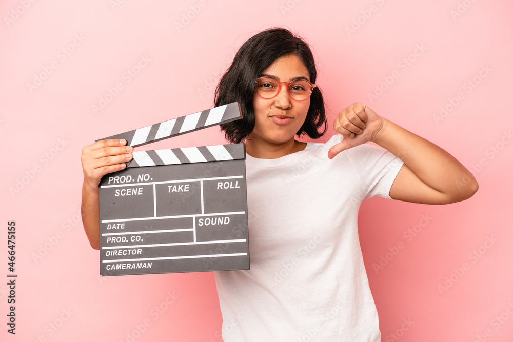 Young latin woman holding clapperboard isolated on pink background feels proud and self confident, example to follow.
