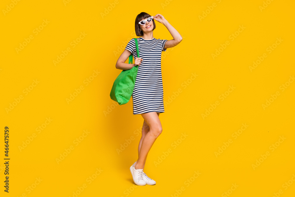 Full length photo of cute brunette millennial lady wear striped dress spectacles bag sneakers isolated on yellow background Full length photo of cute brunette millennial lady wear striped dress spectacles bag sneakers isolated on yellow background