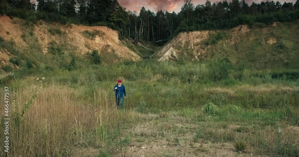 Hiker walks with a backpack in a large, sandy quarry at sunset. The quarry is overgrown with grass and trees. The concept of hiking a healthy lifestyle and weekends in the fresh air Hiker walks with a backpack in a large, sandy quarry at sunset. The quarry is overgrown with grass and trees. The concept of hiking a healthy lifestyle and weekends in the fresh air