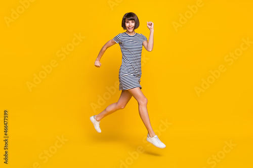 Full body photo of funny young lady run wear striped dress sneakers isolated on yellow background