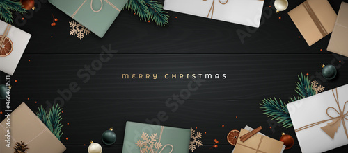 Merry Christmas banner. Flat lay composition with fir tree branch, cinnamon, orange slice, berries, gift craft box, envelope and pine cone on black wooden floor. Scandinavian style.