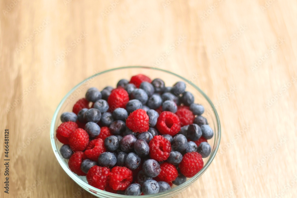 Glass bowl filled with raspberries and blueberries on wooden table. Selective focus. Glass bowl filled with raspberries and blueberries on wooden table. Selective focus.