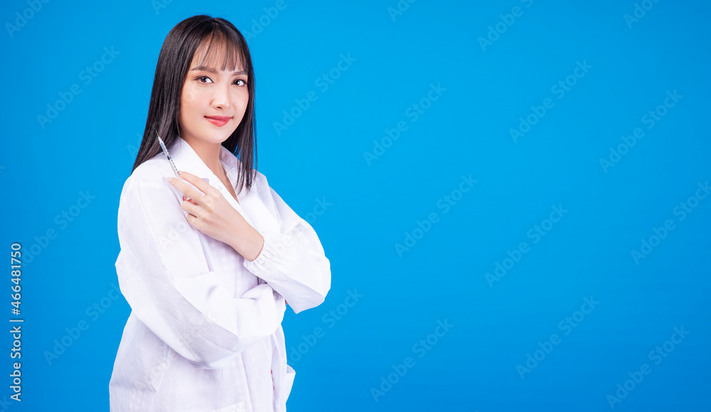 Vaccine immunization disease health care concept. Doctor or nurse young woman wear uniform lab holding and looking syringe in own hands while standing over isolated blue background. Vaccine immunization disease health care concept. Doctor or nurse young woman wear uniform lab holding and looking syringe in own hands while standing over isolated blue background.