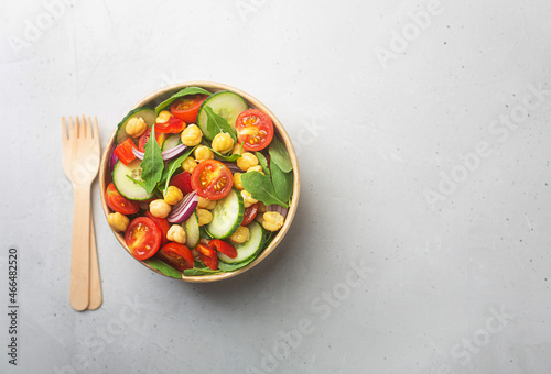 Vegetarian chickpea beans salad prepared with tomatoes and cucumber in a paper bowl with wooden fork