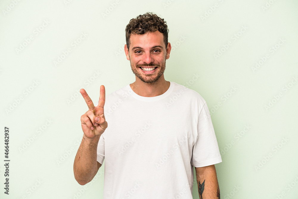 Young caucasian man isolated on green background showing victory sign and smiling broadly. Young caucasian man isolated on green background showing victory sign and smiling broadly.