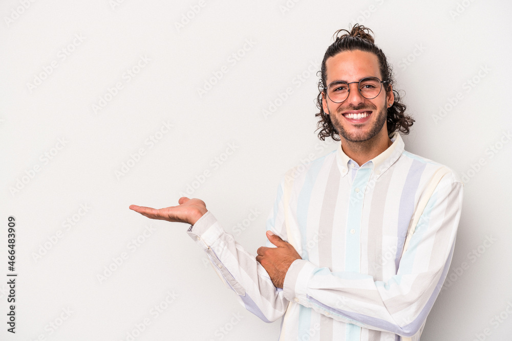 Young caucasian man isolated on gray background showing a copy space on a palm and holding another hand on waist.