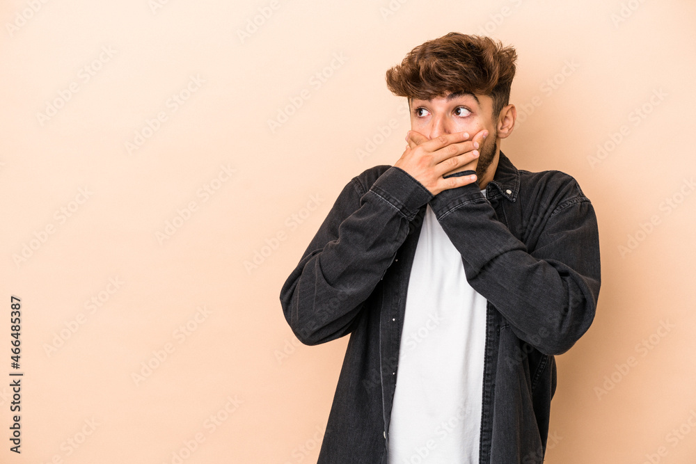 Young arab man isolated on beige background thoughtful looking to a copy space covering mouth with hand. Young arab man isolated on beige background thoughtful looking to a copy space covering mouth with hand.