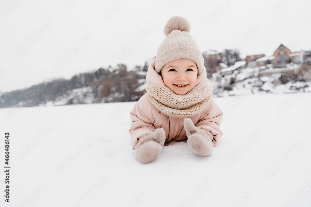 Winter cheerful little child playing throws up snow outdoors. The girl is lying in the snow, playing and having fun. Winter cheerful little child playing throws up snow outdoors. The girl is lying in the snow, playing and having fun.