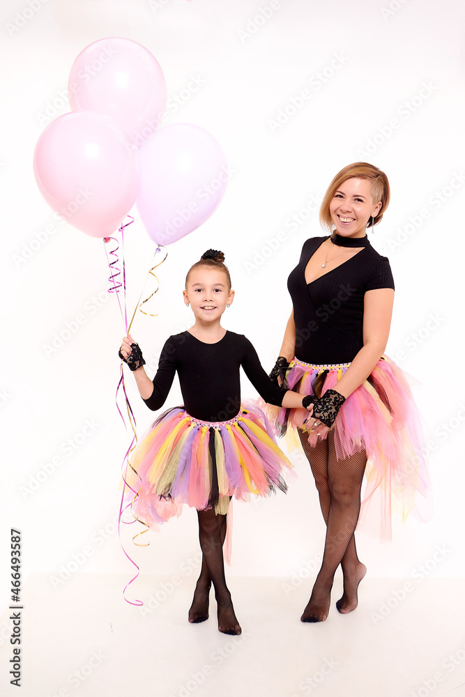 Funny Mother and daughter in same outfits with tutu skirts posing with pink balloons in studio on the white background. Little girl and young mom together Funny Mother and daughter in same outfits with tutu skirts posing with pink balloons in studio on the white background. Little girl and young mom together
