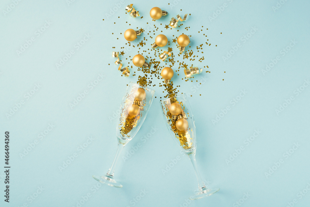 Top view photo of splash of gold christmas decorations from two champagne glasses on isolated pastel blue background - obrazy, fototapety, plakaty 