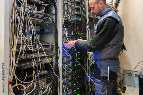 Maintenance of a rack with powerful network servers in the data center. The technician is connecting the fiber backbone wires to the network interfaces.