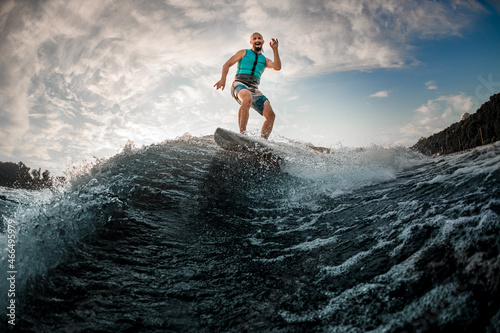 cheerful man wakesurfer having fun and balancing on wakeboard along the river wave