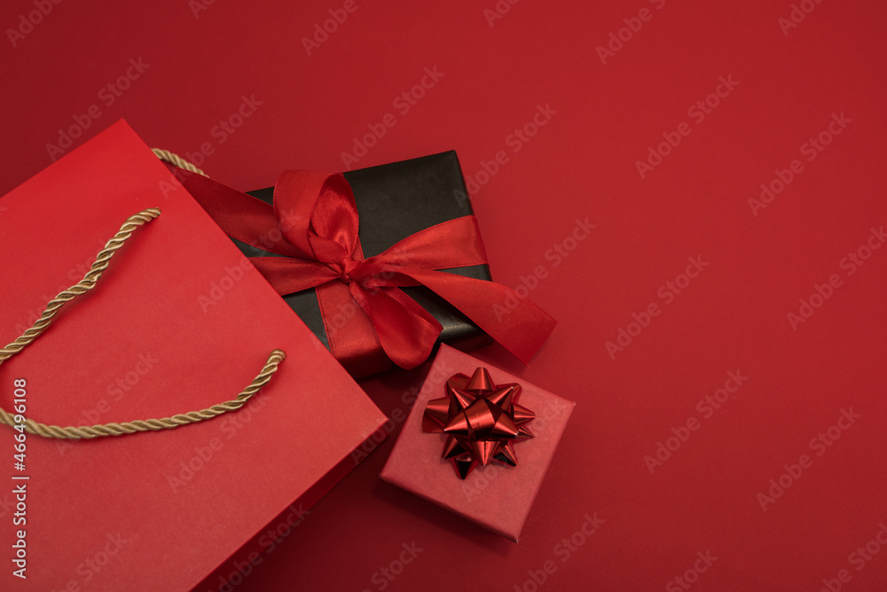Creative look, two red and black gift boxes and a red shopping bag on a red background. Black Friday, discounts, sales, Christmas shopping on a red background, a place for text, a black gift box with Creative look, two red and black gift boxes and a red shopping bag on a red background. Black Friday, discounts, sales, Christmas shopping on a red background, a place for text, a black gift box with