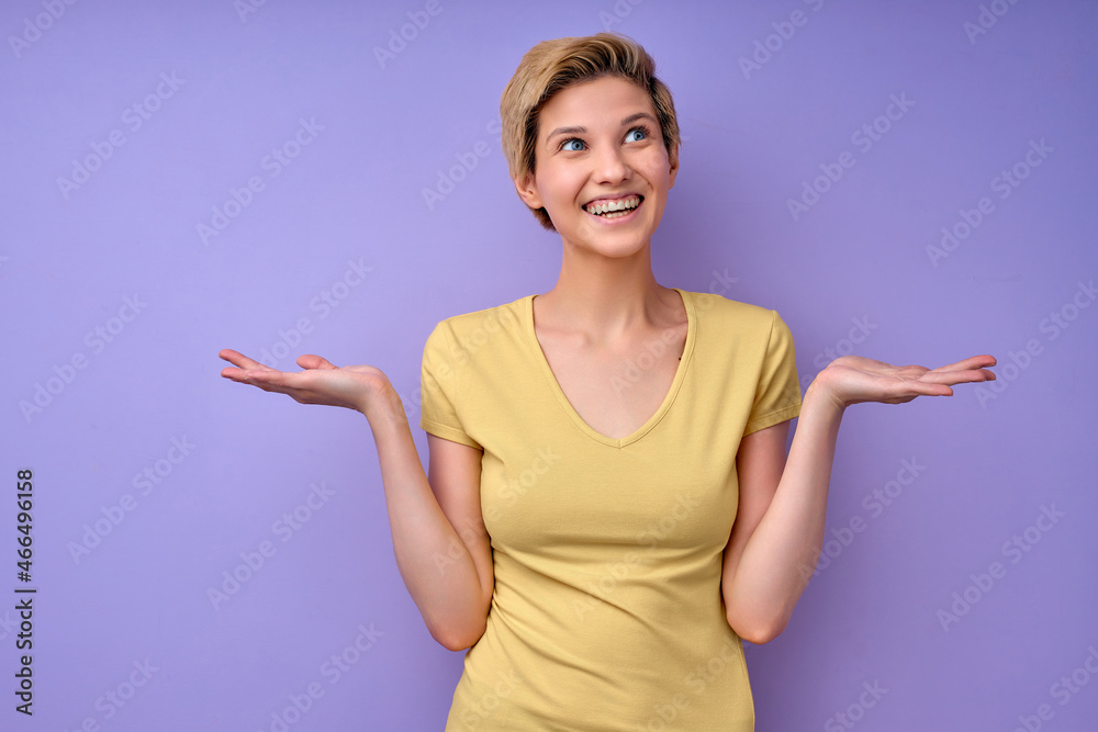 Funny caucasian female spreading arms don't know expression, isolated on purple studio background. Young lady in casual yellow t-shirt posing, misunderstanding, raising arms at side. copy space Funny caucasian female spreading arms don't know expression, isolated on purple studio background. Young lady in casual yellow t-shirt posing, misunderstanding, raising arms at side. copy space
