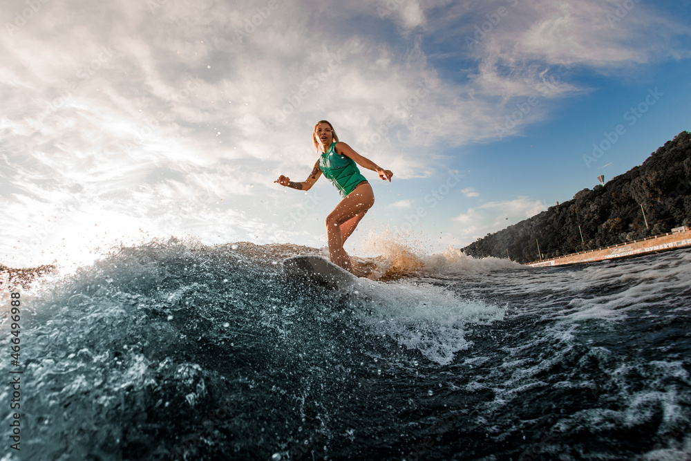 athletic woman in a turquoise vest on wakeboard actively riding the river wave