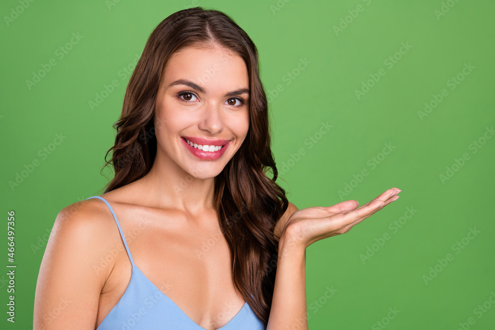 Photo of young attractive woman happy positive smile hold hand product offer advertising isolated over green color background Photo of young attractive woman happy positive smile hold hand product offer advertising isolated over green color background