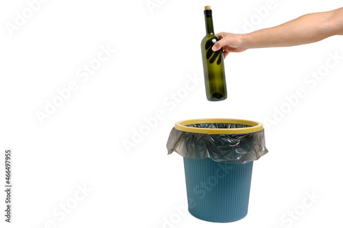In hand, an empty glass wine bottle is thrown into trash.