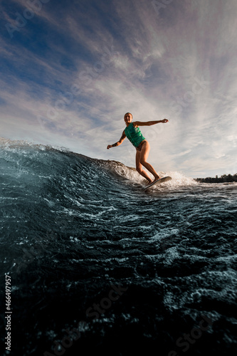 female wakesurfer vigorously riding on wakeboard down the river waves against the blue sky.