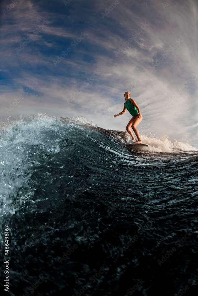 Active female wakesurfer riding on wakeboard down the river waves against the blue sky. Active female wakesurfer riding on wakeboard down the river waves against the blue sky.