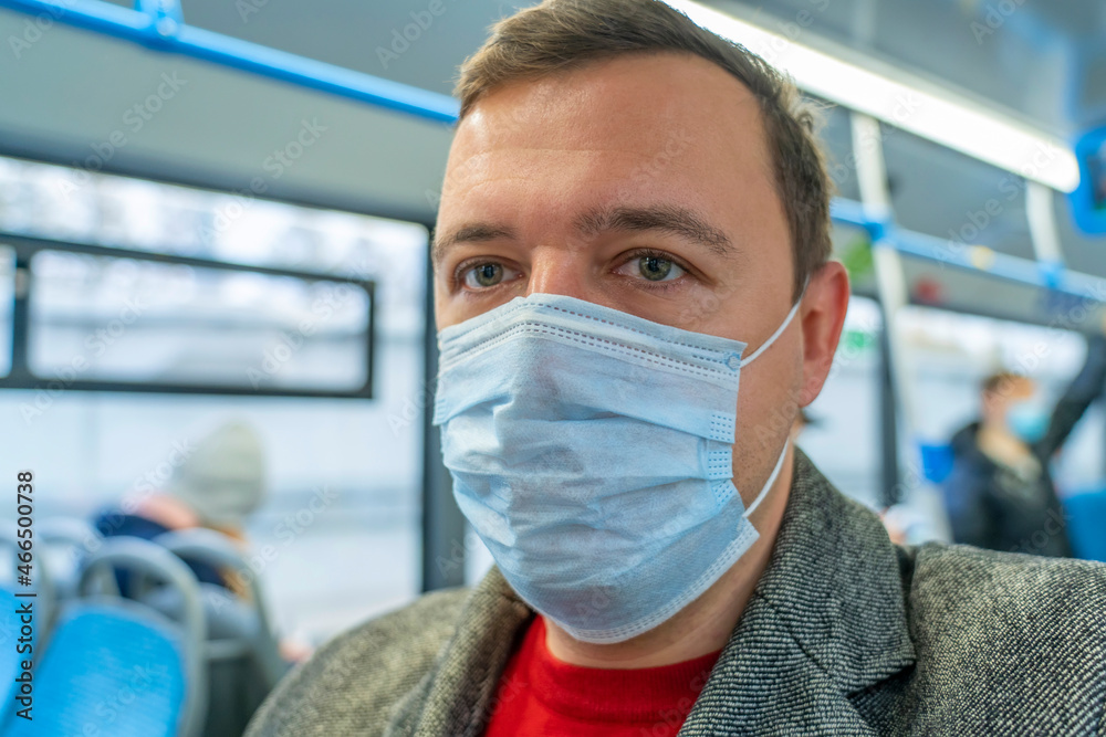 Portrait of male passenger wearing medical face mask in public transportation. Millennial man looking away at window, thinking, going to work by bus during coronavirus pandemic. Themes social distance
