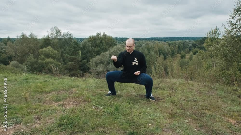 Middle aged Caucasian man practices wushu in the summer in a park on a hill. Traditional Chinese gymnastics qigong and Tai chi. Meditation and relaxation in nature. Healthy lifestyle and sports Middle aged Caucasian man practices wushu in the summer in a park on a hill. Traditional Chinese gymnastics qigong and Tai chi. Meditation and relaxation in nature. Healthy lifestyle and sports