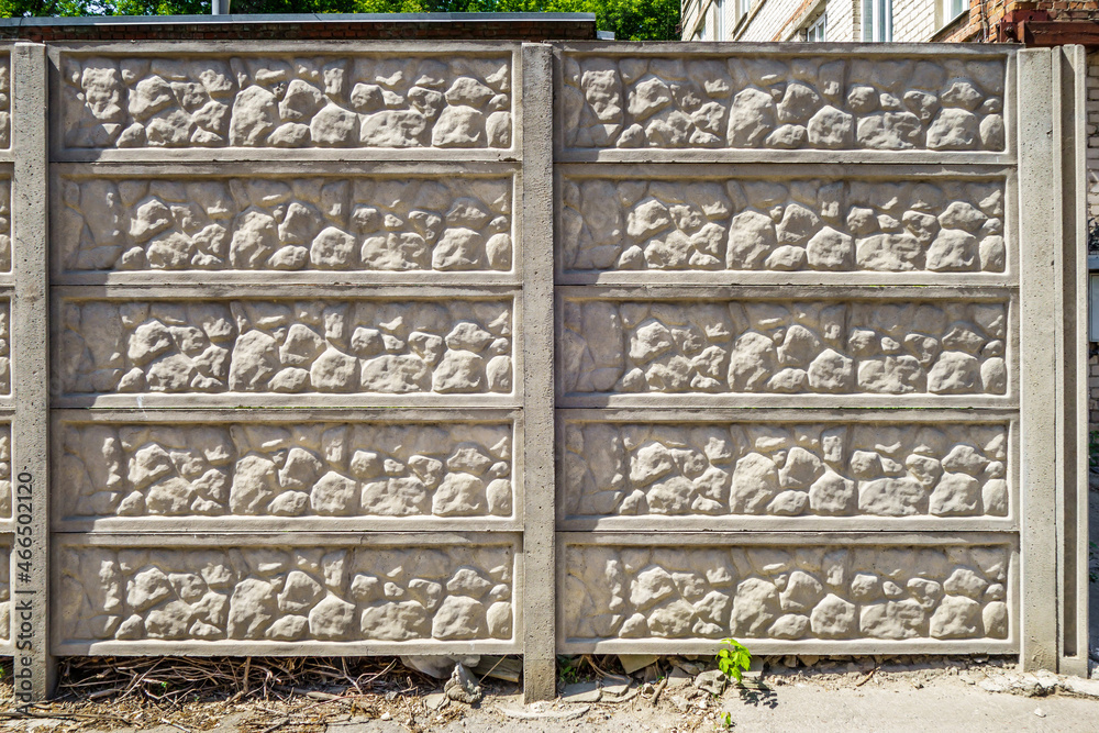 Front view of a concrete fence, divided by sections imitating stone masonry
