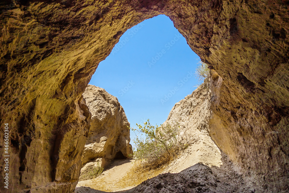View of bright summer day and blue sky from darkness of cave. This is entrance to underground tunnel of Buddhist settlement of I-V centuries on Kara-Tepe hill, Termez, Uzbekistan