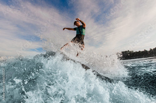 energetic man wakesurfer riding down the blue splashing wave on a warm day