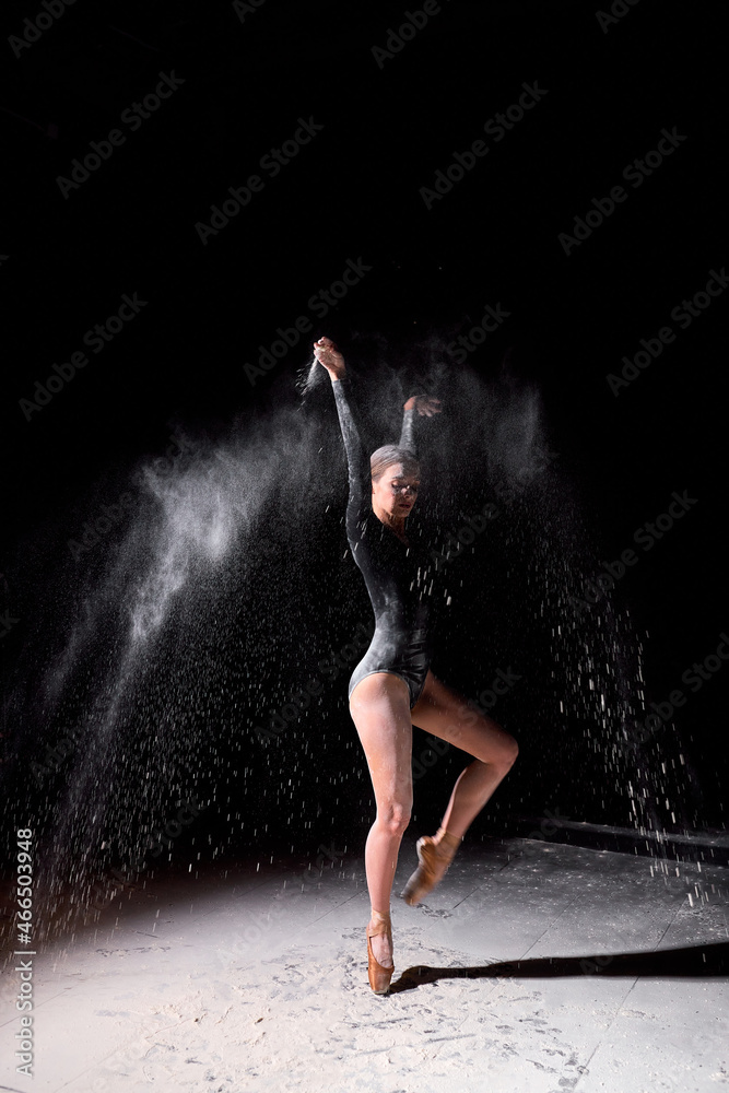 Beautiful pretty female wearing black gymnastic bodysuit dancing with flying powder flour, full-length portrait of attractive caucasian lady in slow motion. people, dance, art concept