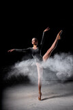 Dancer posing dancing gracefully in studio with cloud of dust, flour. flexible Dancer in black suit is moving, in action, having good choreographic training, raising leg up. ballet, performance
