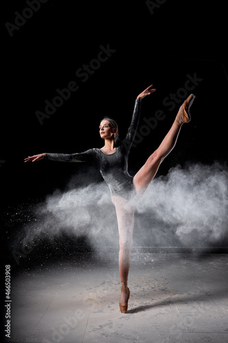 Dancer posing dancing gracefully in studio with cloud of dust, flour. flexible Dancer in black suit is moving, in action, having good choreographic training, raising leg up. ballet, performance