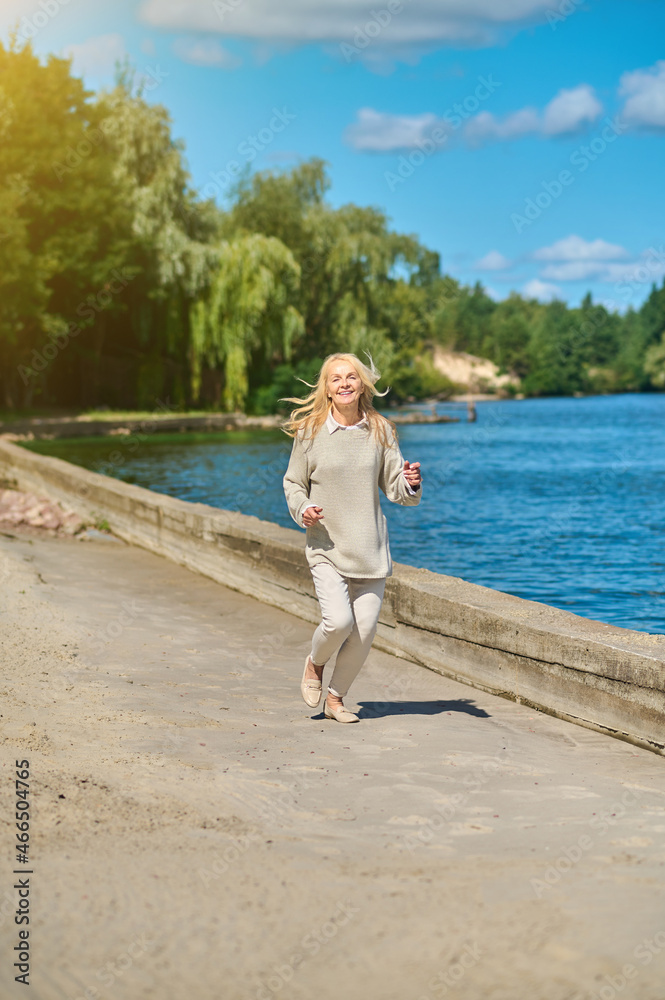 Smiling woman in casual clothes running near sea