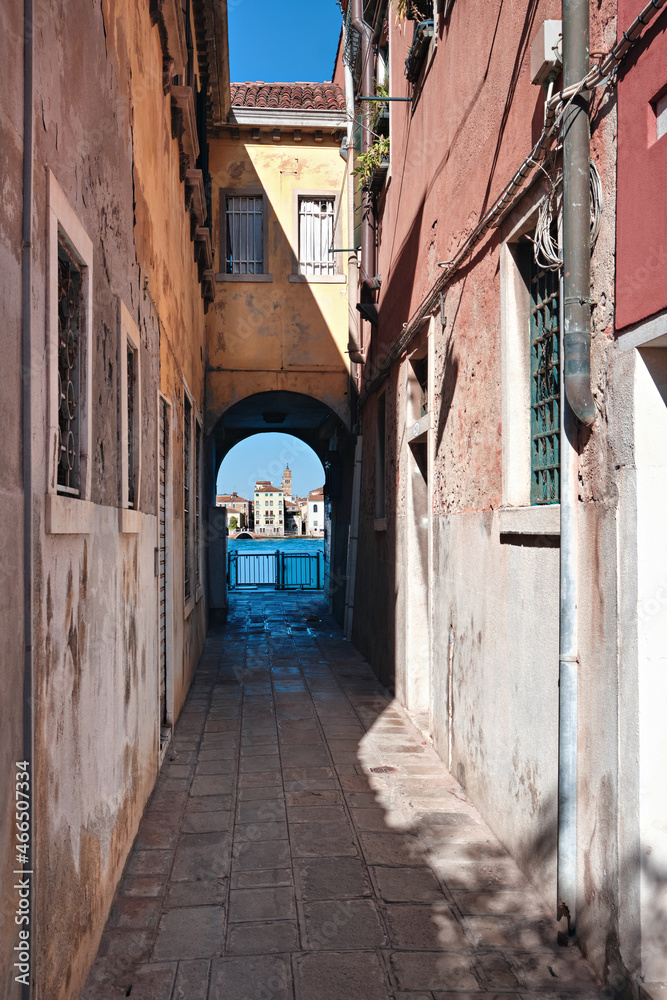 Narrow street in Giudecca, island in Venetian lagoon. Historic houses form an arch passageway leading towards canal and historic houses on the other side across the water.