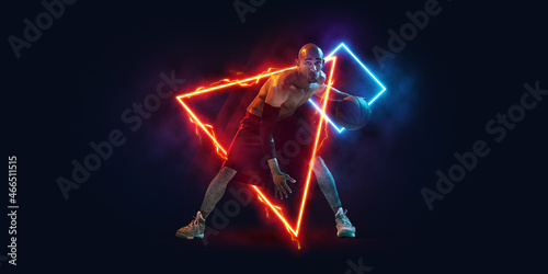 Poster. Sportive young man, professional basketball player in motion and action with ball isolated on dark background with neoned geometric figure photo