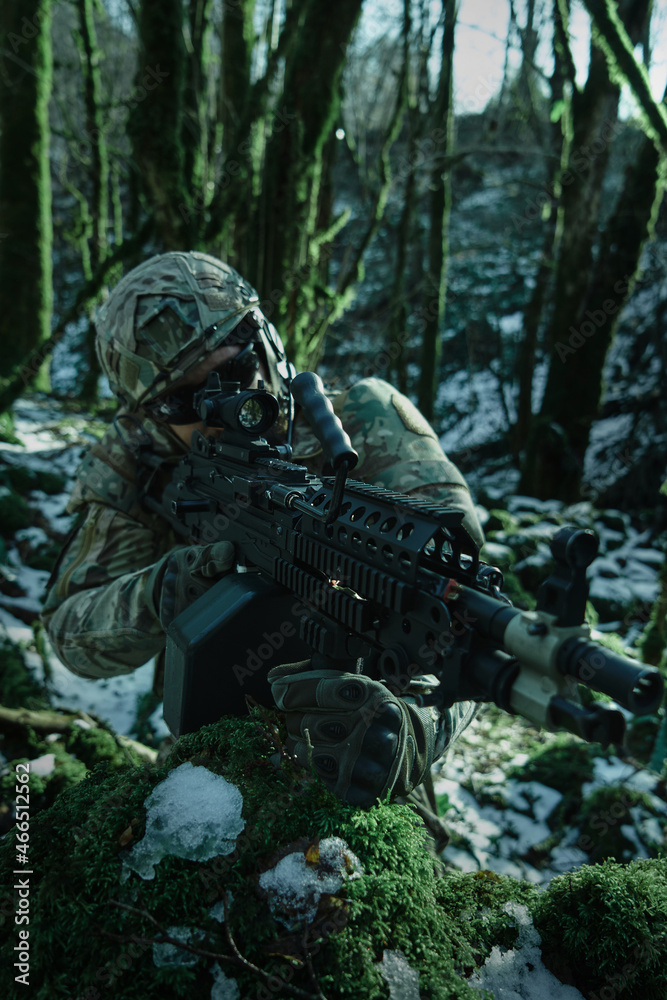 Portrait of airsoft player in professional equipment in helmet aiming at victim with gun in the forest. Soldier with weapons at war