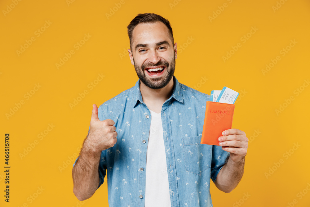 Traveler tourist man 20s wear blue shirt hold passport boarding tickets show thumb up isolated on plain yellow background studio Passenger travel abroad weekends getaway. Air flight journey concept. Traveler tourist man 20s wear blue shirt hold passport boarding tickets show thumb up isolated on plain yellow background studio Passenger travel abroad weekends getaway. Air flight journey concept.