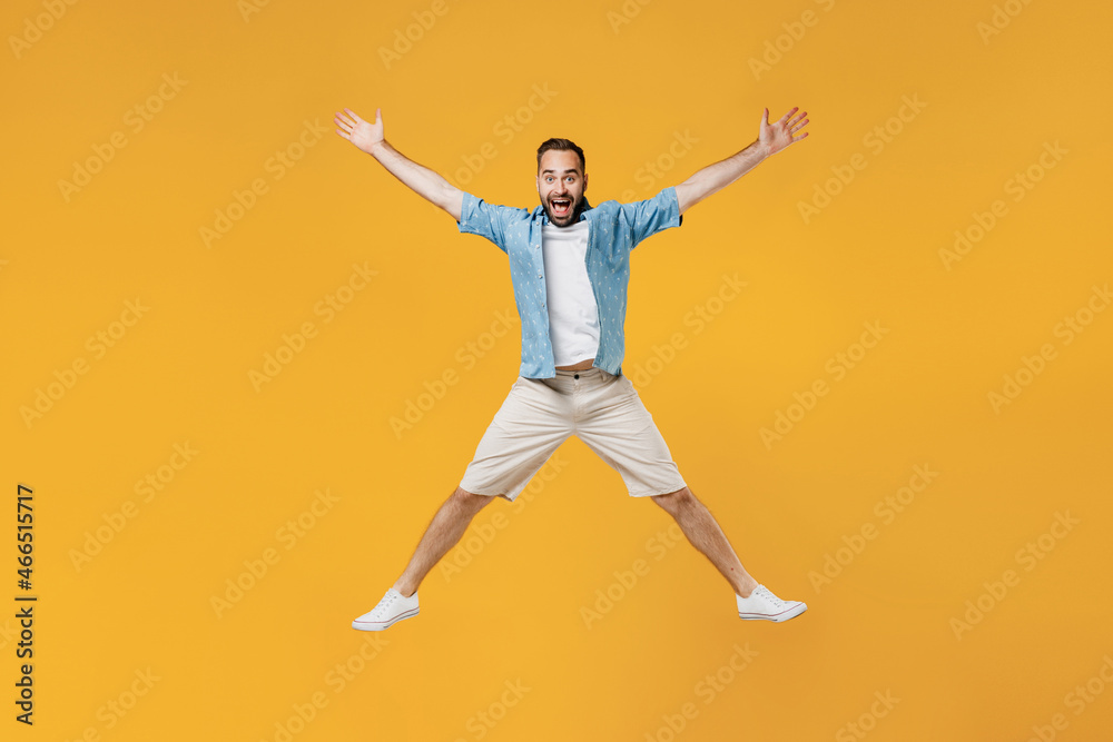 Full body young smiling happy caucasian man 20s wearing blue shirt white t-shirt jump high with outstretched hands scream isolated on plain yellow background studio portrait. People lifestyle concept.