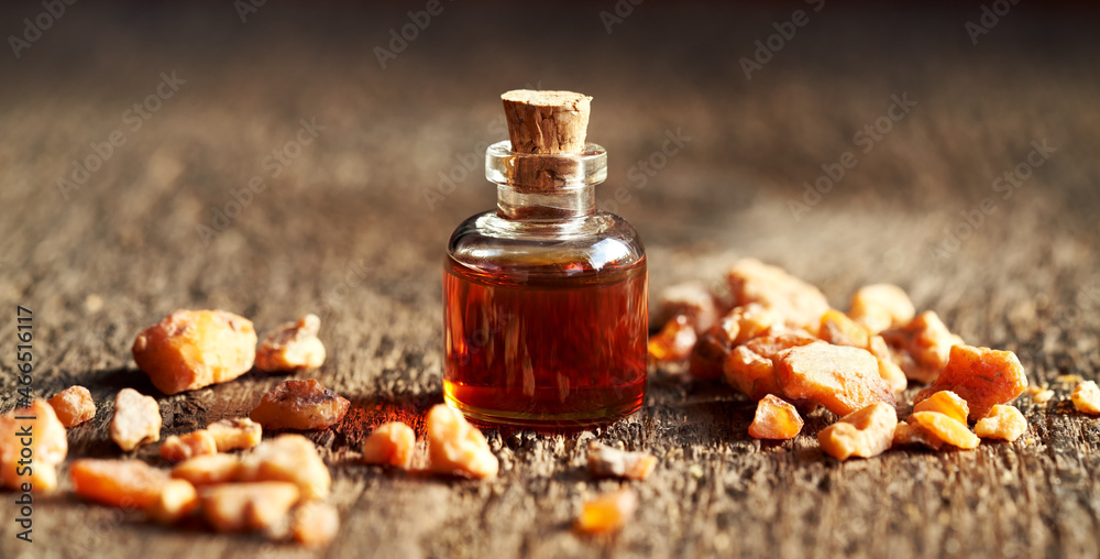 A bottle of styrax essential oil with benzoin resin on a wooden table A bottle of styrax essential oil with benzoin resin on a wooden table