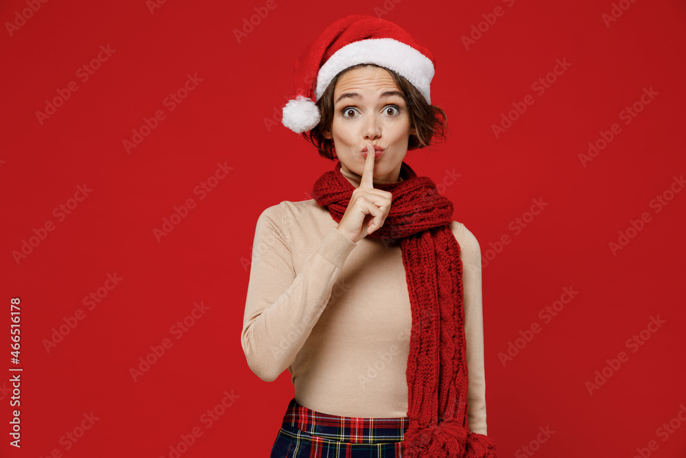 Young smiling woman 20s wear Santa Claus Christmas red hat say hush be quiet with finger on lips shhh gesture isolated on plain red background studio portrait. Happy New Year 2022 celebration concept. Young smiling woman 20s wear Santa Claus Christmas red hat say hush be quiet with finger on lips shhh gesture isolated on plain red background studio portrait. Happy New Year 2022 celebration concept.