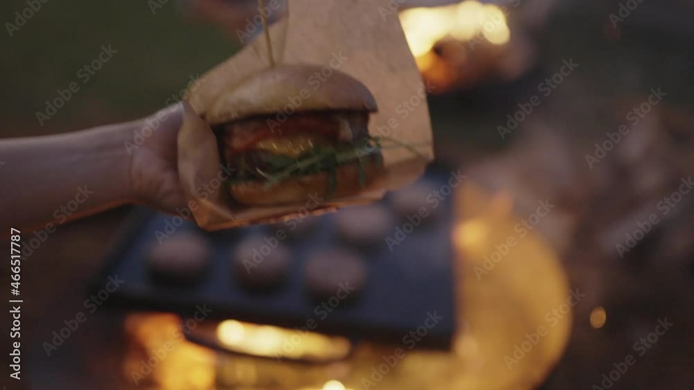 Hands holding beef burger with fire in the background Hands holding beef burger with fire in the background