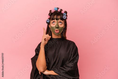 Young mixed race woman waiting in a Beaty salon isolated on pink background pointing upside with opened mouth. © Asier