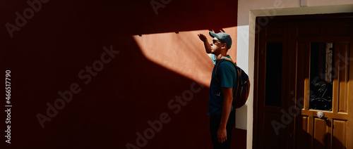 Man traveller standing near red urban wall with hard sunlight and dark shadows. Traveler concept