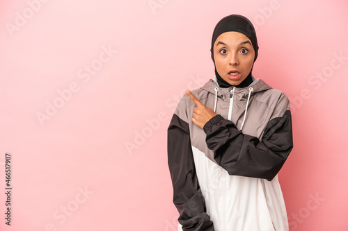 Young Arab woman with sport burqa isolated on pink background pointing to the side