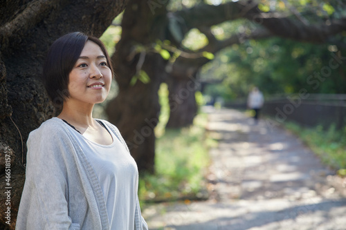 早朝の新緑の中でほほ笑む40代日本人女性
