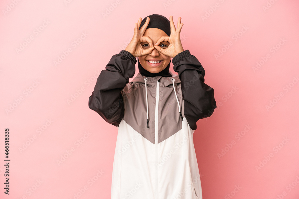 Young Arab woman with sport burqa isolated on pink background showing okay sign over eyes Young Arab woman with sport burqa isolated on pink background showing okay sign over eyes