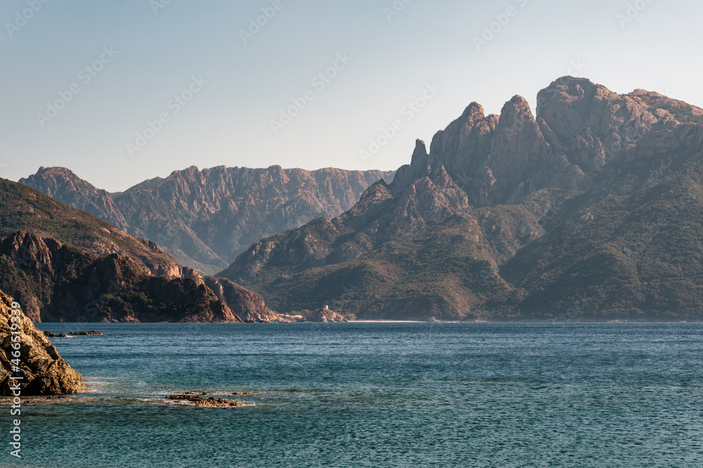 Genoese tower and beach at Porto on the west coast of Corsica with dramatic rocky mountains behind and Mediterranean in the foreground