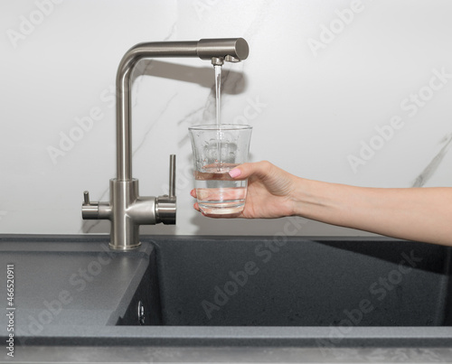 Woman pouring filtered purified water from tap into glass in kitchen. clean water and healthy life concept. closeup